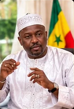 Chérif Moussa en tenue blanche, devant un drapeau